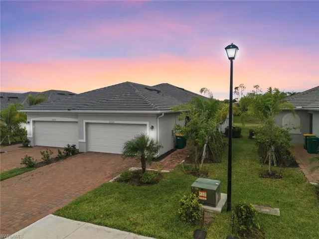 View of front of property featuring a garage, decorative driveway, a lawn, stucco siding, and a tiled roof