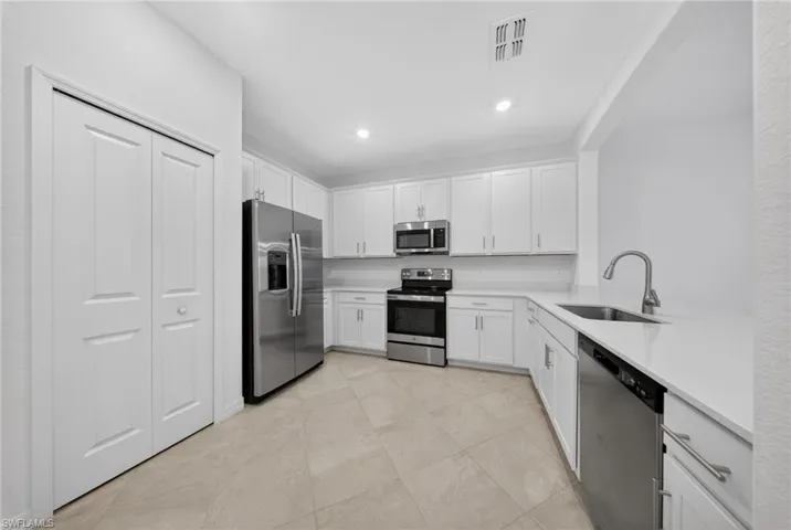 Kitchen featuring stainless steel appliances, white cabinets, light stone counters, and recessed lighting