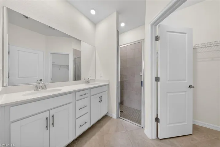 Full bath featuring a walk in closet, double vanity, a shower stall, light tile patterned floors, and recessed lighting