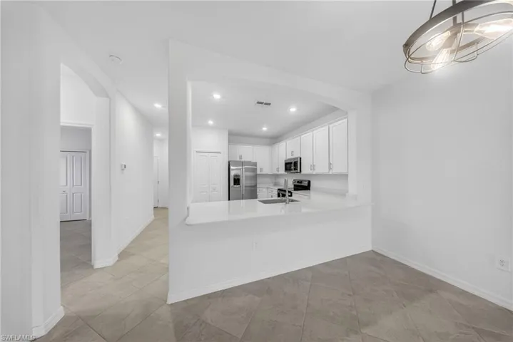 Kitchen with arched walkways, white cabinets, stainless steel appliances, a peninsula, and light stone countertops