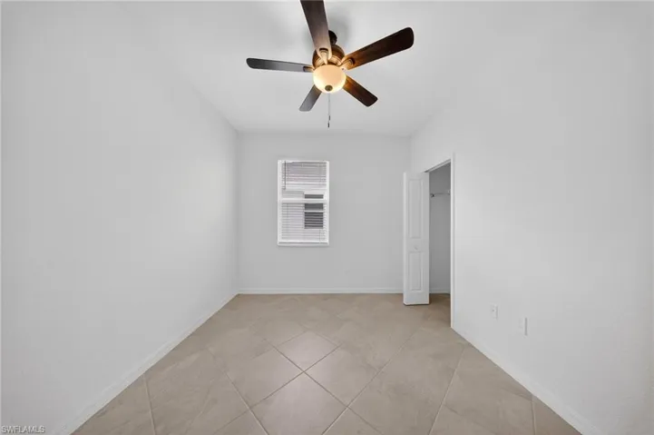 Unfurnished bedroom featuring ceiling fan, light tile patterned flooring, and a spacious closet