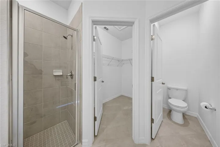 Bathroom with a spacious closet, a shower stall, and light tile patterned floors