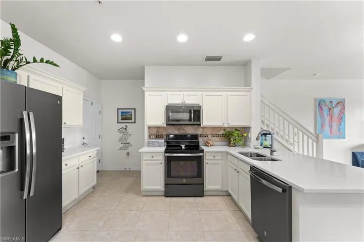 Kitchen with white cabinets, kitchen peninsula, appliances with stainless steel finishes, and sink