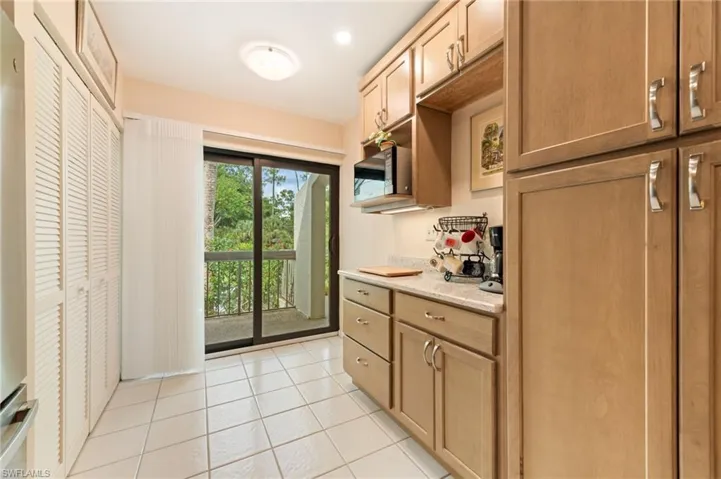 Kitchen featuring light wood-finish cabinetry, stone-style countertops, ceramic tile flooring, floor-to-ceiling louvered-panel cabinetry, and a sliding glass door providing external access