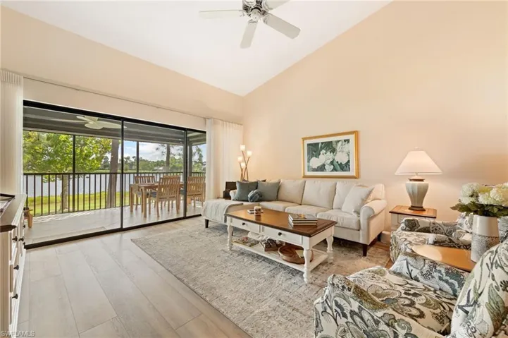 Living area featuring vaulted ceilings, CoreTec luxury vinyl plank flooring, ceiling fan, and sliding glass doors opening to a screened lanai with water scenery