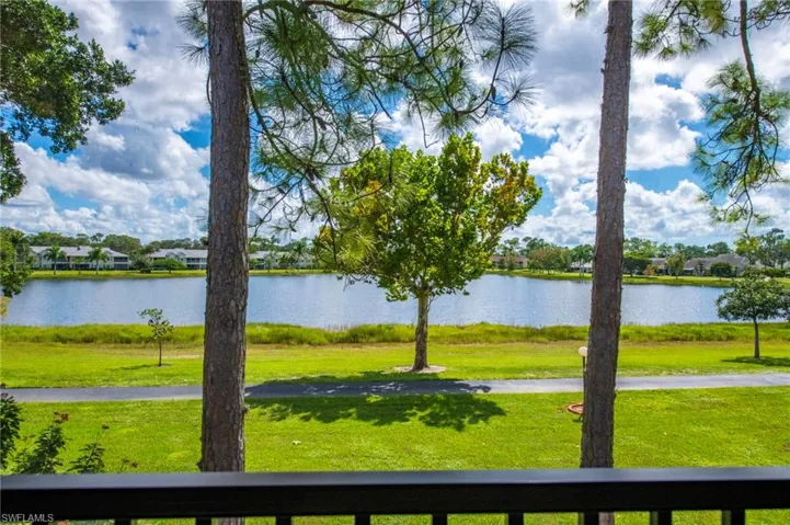 Waterfront scenery featuring a lake, expansive grass grounds, mature trees, and a paved walkway