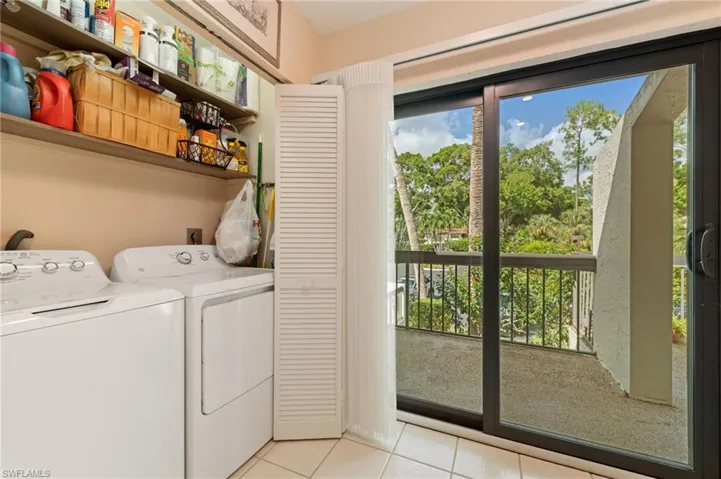 Laundry area in between Kitchen and front porch slider, featuring built-in overhead shelving, louvered closet doors, tile flooring, and sliding glass doors to a railed balcony