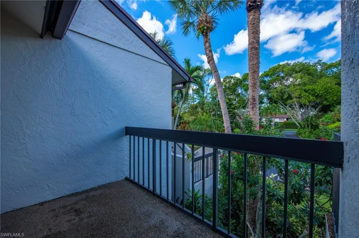 Covered exterior balcony featuring a textured stucco finish, dark metal railing, and exposed aggregate flooring