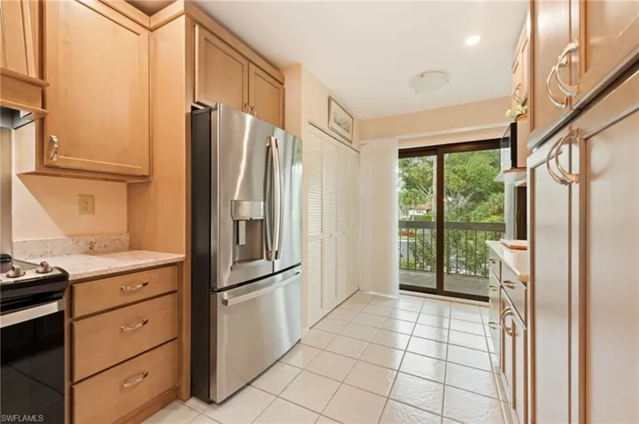 Kitchen featuring light wood cabinetry, stone countertops, stainless steel refrigerator, tiled flooring, and sliding glass doors with balcony access