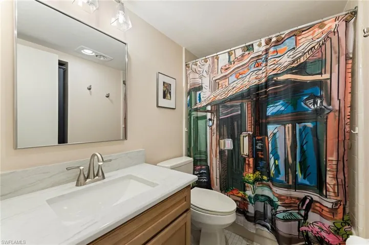 Bathroom featuring a wood-finish vanity with a stone-composite countertop, undermount sink, brushed nickel faucet, and a large frameless rectangular wall mirror