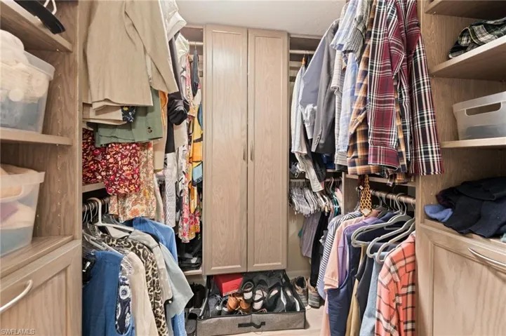 Primary custom walk-in closet featuring floor-to-ceiling wood-finish cabinetry, built-in shelving units, integrated clothing rods, and centrally located double-door storage