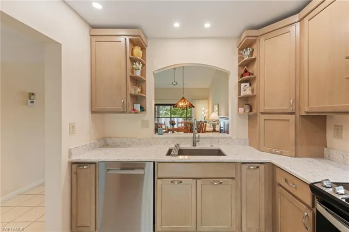 Kitchen featuring light wood cabinetry with built-in open shelving, light-toned stone-patterned countertops, a stainless steel undermount sink, and recessed ceiling lighting