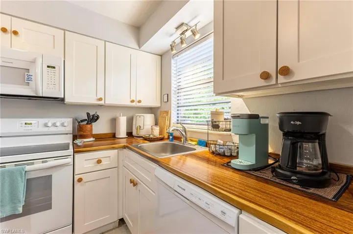 Kitchen featuring white appliances, white cabinetry, and wooden counters