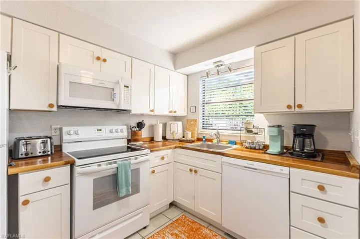 Kitchen featuring white appliances, wood counters, white cabinets, and light tile patterned floors
