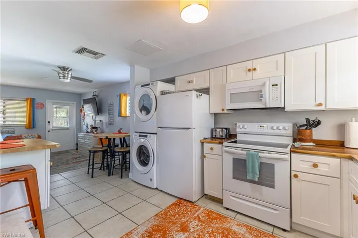 Kitchen with white appliances, light tile patterned floors, butcher block countertops, stacked washing machine and dryer, and white cabinets