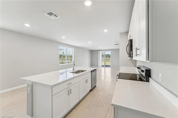 Kitchen with stainless steel appliances, sink, a center island with sink, and white cabinets