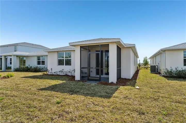 Rear view of house with central AC unit, a sunroom, and a lawn