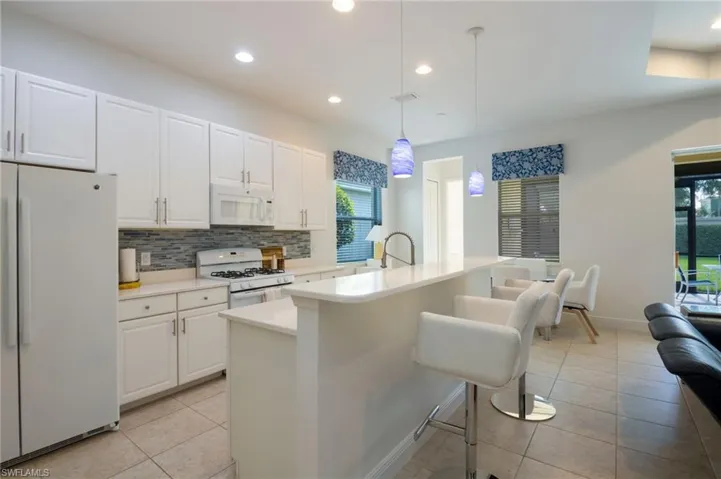 Modern kitchen featuring white cabinetry, light countertops, a tile backsplash, stainless steel sink, and pendant lighting