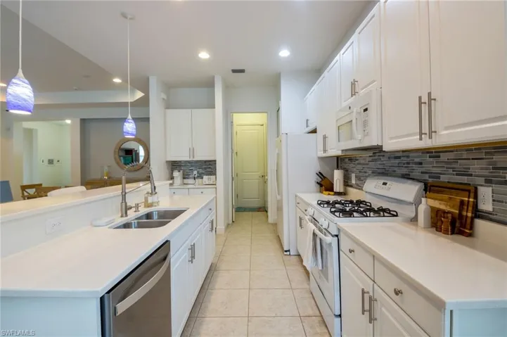 Kitchen island with a double basin stainless steel sink, stainless steel dishwasher, and white cabinetry