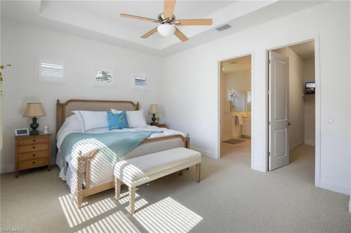 Spacious room featuring a tray ceiling with a ceiling fan, a large window with blinds, and light-colored carpet flooring