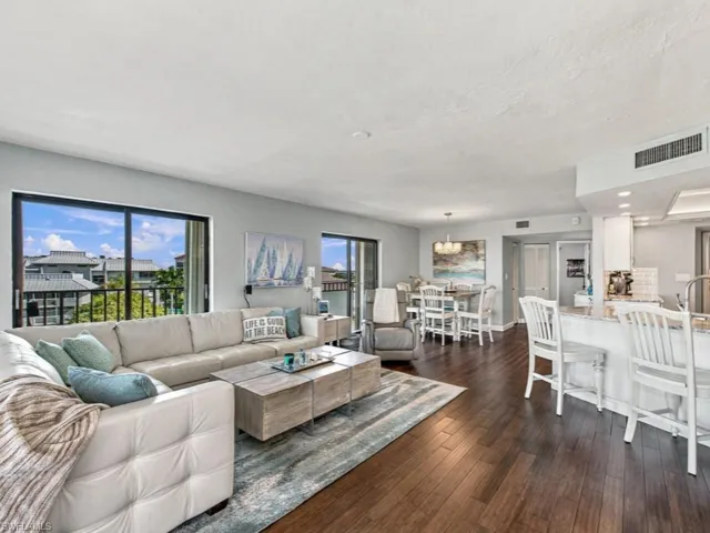 Open-concept living space featuring wood-finish flooring, dual glass sliding doors, and a kitchen peninsula with stone-finish countertops