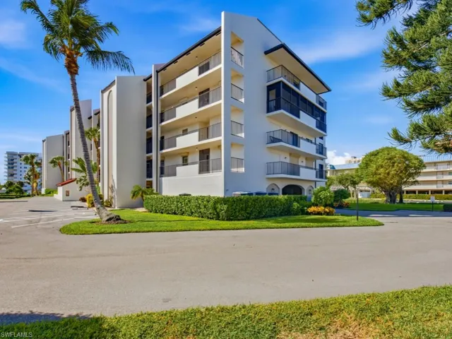 Multi-story exterior featuring white stucco siding, private balconies with metal railings, and manicured perimeter landscaping