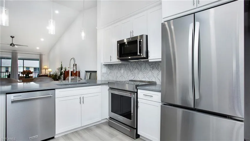 Kitchen with appliances with stainless steel finishes, a sink, decorative backsplash, dark countertops, and lofted ceiling