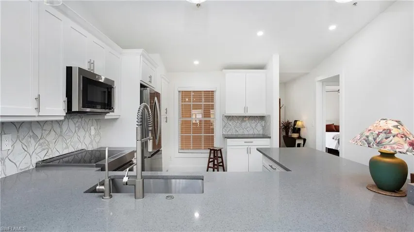 Kitchen with stainless steel microwave, recessed lighting, white cabinets, backsplash, and stove