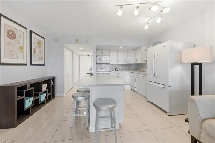 Kitchen with white appliances, a kitchen breakfast bar, white cabinets, decorative backsplash, and a kitchen island