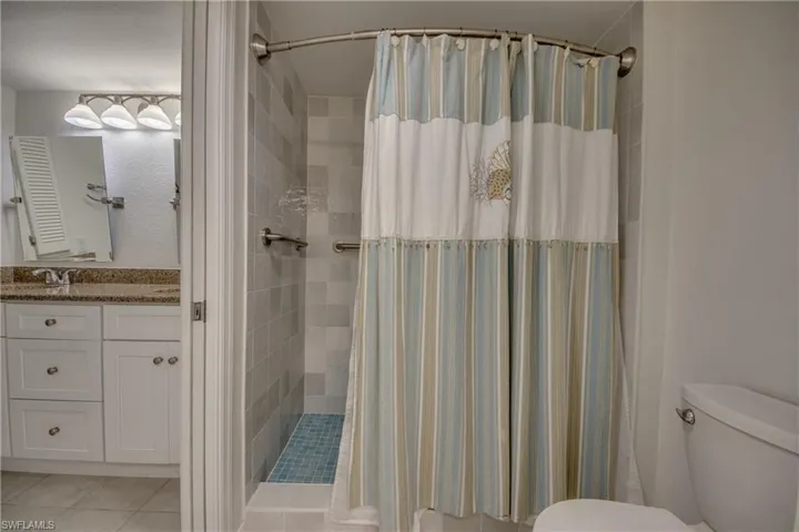 Bathroom with a shower with curtain, vanity, toilet, and tile flooring