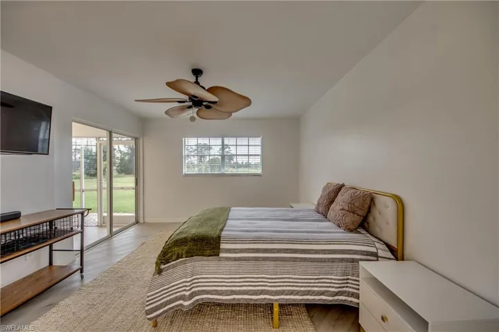 Bedroom featuring ceiling fan, wood-look tile floors, multiple windows, and sliding door to lanai