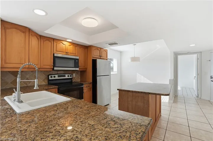 Kitchen with brown cabinetry, a kitchen island, stainless steel appliances, light tile patterned flooring, and hanging light fixtures