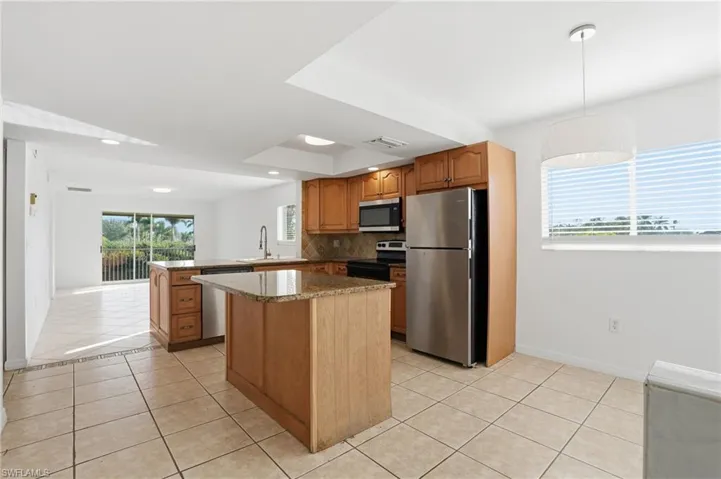 Kitchen with stainless steel appliances, brown cabinets, light tile patterned floors, dark stone counters, and healthy amount of natural light