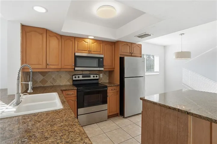 Kitchen featuring appliances with stainless steel finishes, hanging light fixtures, dark stone counters, light tile patterned floors, and backsplash