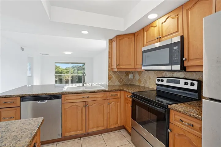 Kitchen with appliances with stainless steel finishes, recessed lighting, dark stone countertops, light tile patterned floors, and decorative backsplash