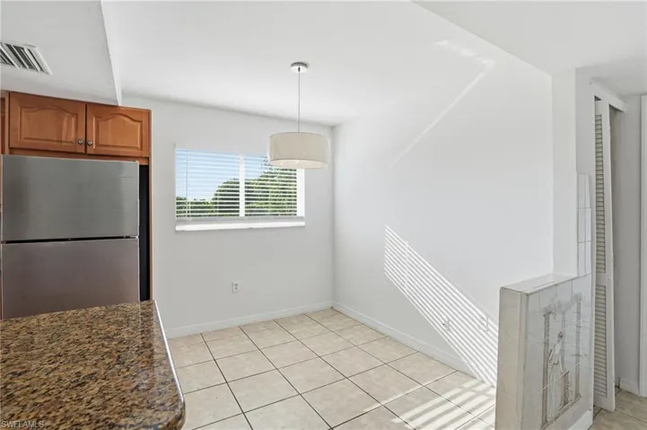 Kitchen featuring freestanding refrigerator, brown cabinets, decorative light fixtures, light tile patterned floors, and dark stone countertops
