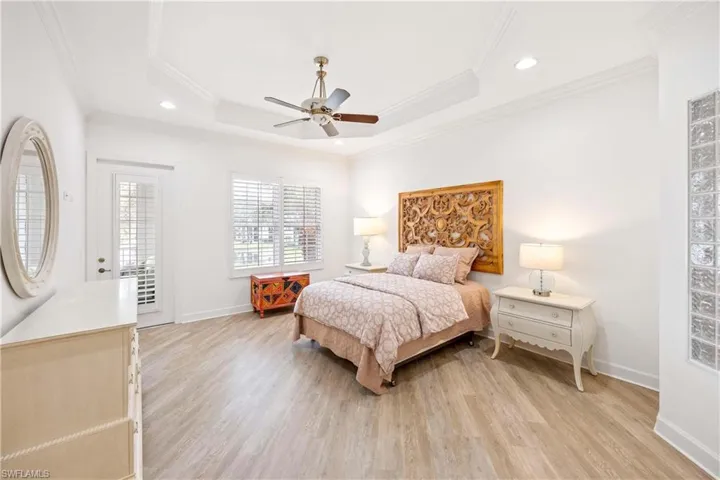 Bedroom with light wood-type flooring, crown molding, a raised ceiling, a ceiling fan, and recessed lighting