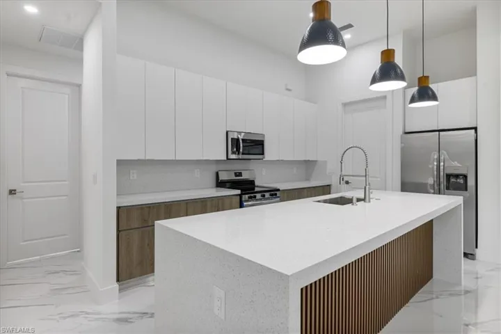Kitchen featuring decorative light fixtures, white cabinets, stainless steel appliances, and a center island with sink