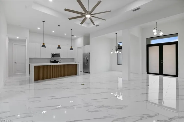 Kitchen with a large island with sink, pendant lighting, stainless steel appliances, and white cabinetry