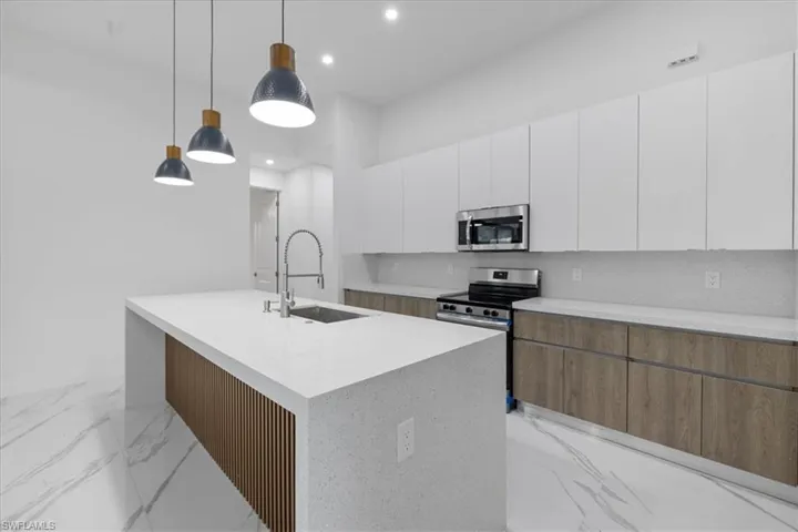 Kitchen with pendant lighting, decorative backsplash, sink, white cabinetry, and appliances with stainless steel finishes