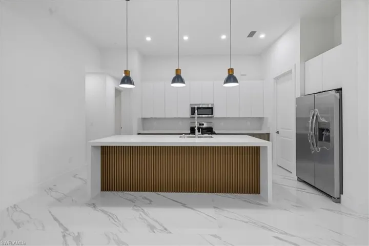 Kitchen with appliances with stainless steel finishes, a kitchen island with sink, white cabinetry, and decorative light fixtures