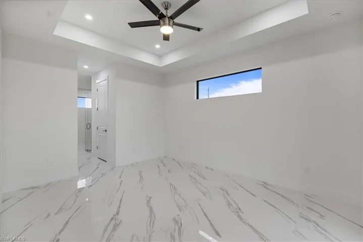 Unfurnished room featuring ceiling fan, plenty of natural light, and a tray ceiling