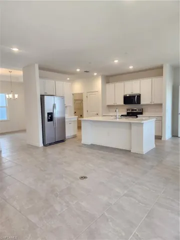 Kitchen with fridge, white cabinets, an island with sink, and stove
