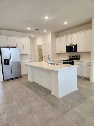 Kitchen featuring fridge, range, a kitchen island with sink, white cabinets, and recessed lighting