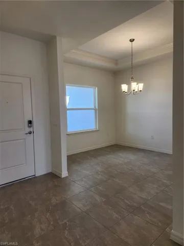 Foyer entrance with a raised ceiling, ornamental molding, and a chandelier
