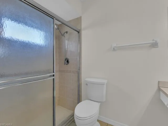 Shower with textured glass sliding doors and a chrome shower head, complemented by neutral-toned wall tiles