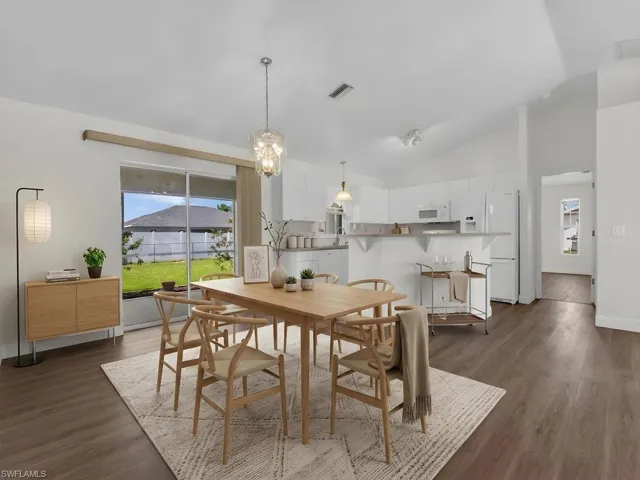 Open-concept dining area featuring wood-finish flooring, vaulted ceilings, and a glass sliding door to the backyard