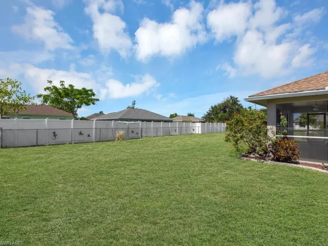 Expansive backyard featuring a lush lawn, white privacy fencing, and mature landscaping