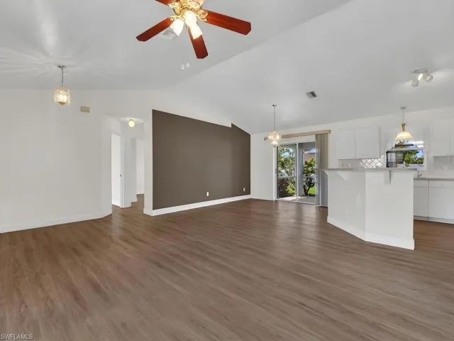 Spacious open-concept interior featuring vaulted ceilings, wood-finish flooring, and a kitchen with white cabinetry and an integrated island