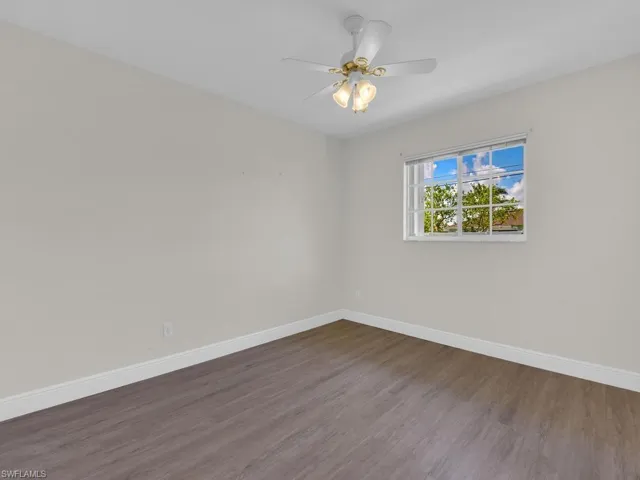 Interior room featuring a single window, a ceiling fan with integrated lighting, wood-finish flooring, and white baseboards